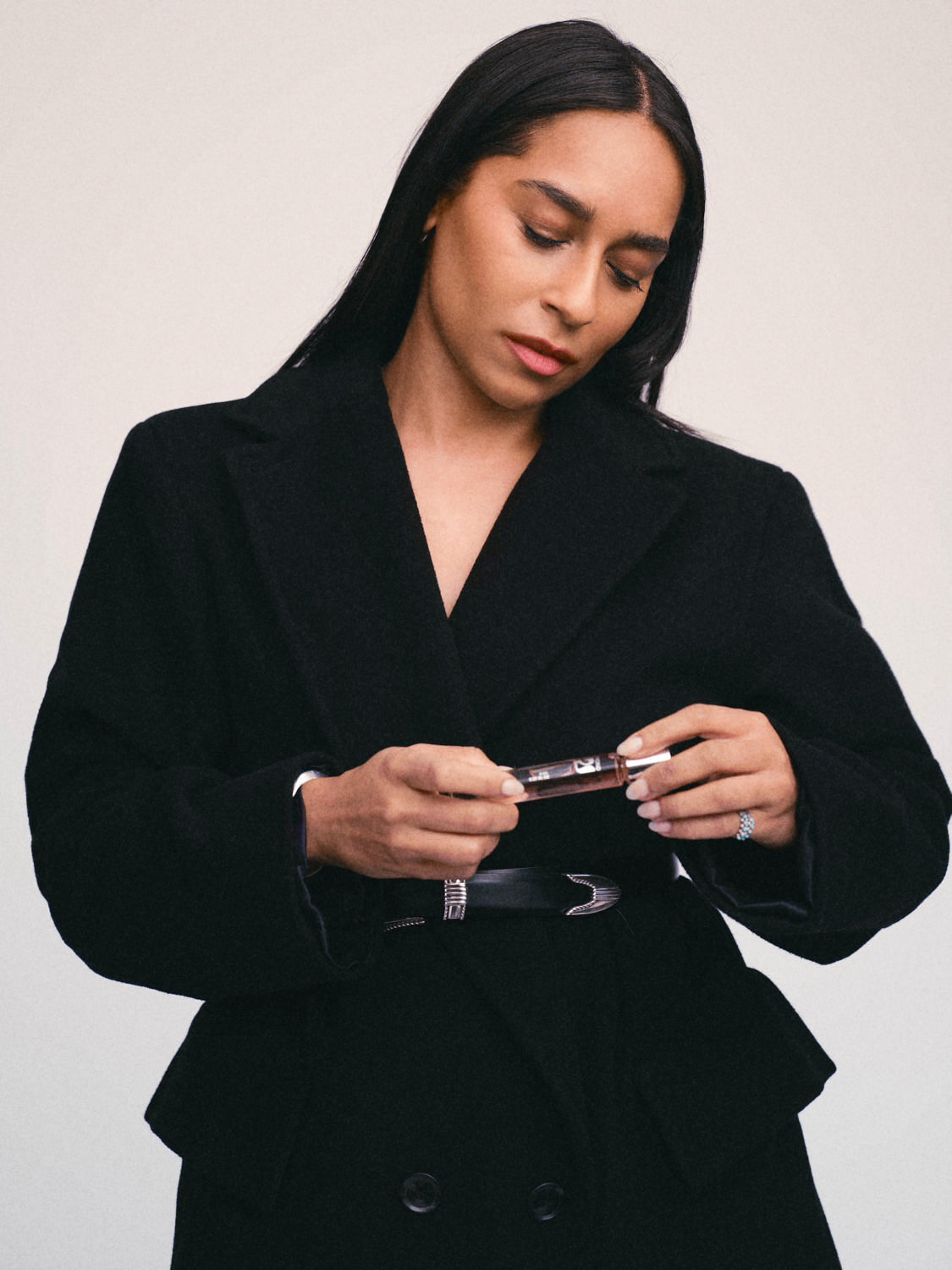 Ayond founder Shani van Breukelen holding a perfume oil rollerball in a black suit with a sliver belt.