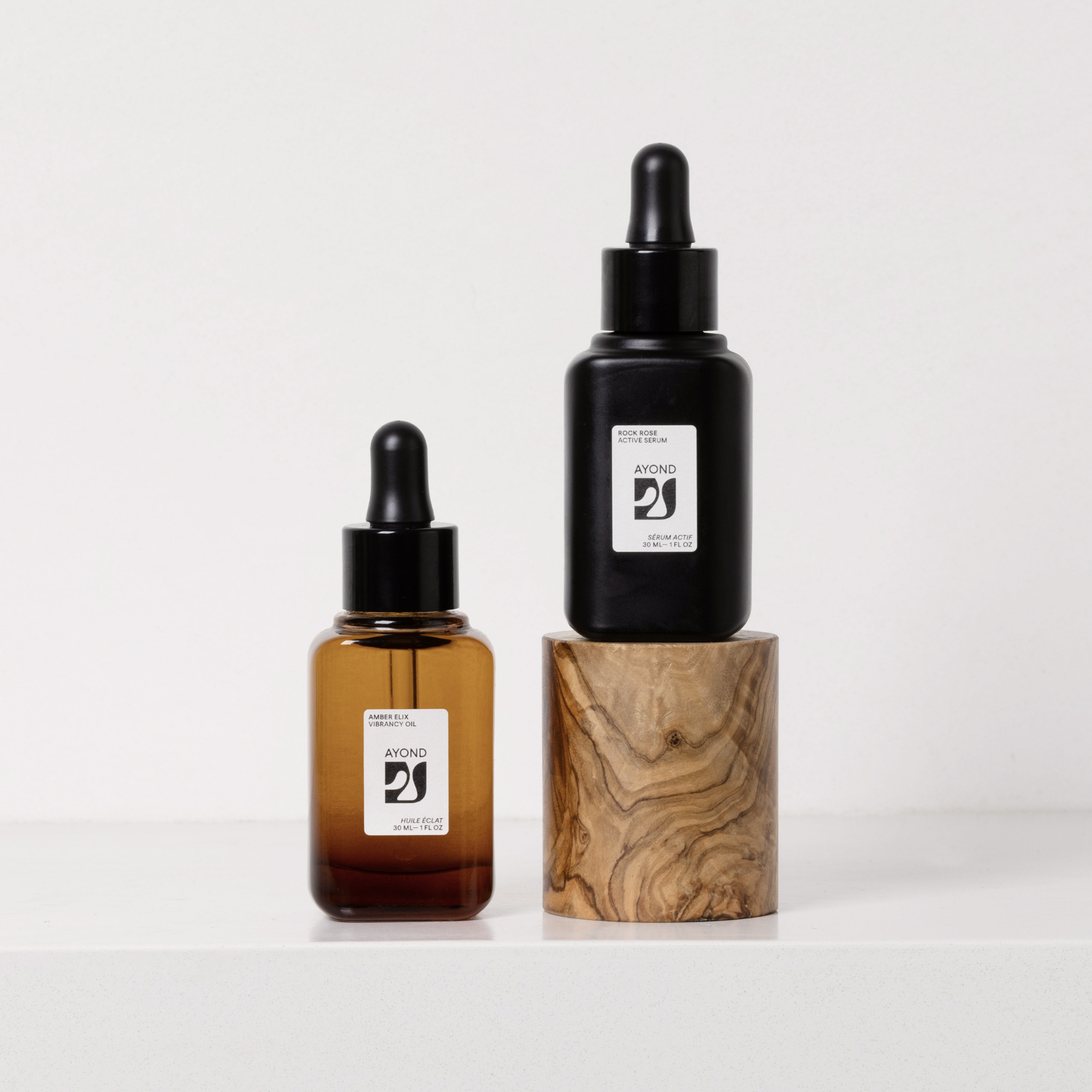 Amber Elix Vibrancy Oil and Rock Rose Active Serum dropper bottles on an olive wood block