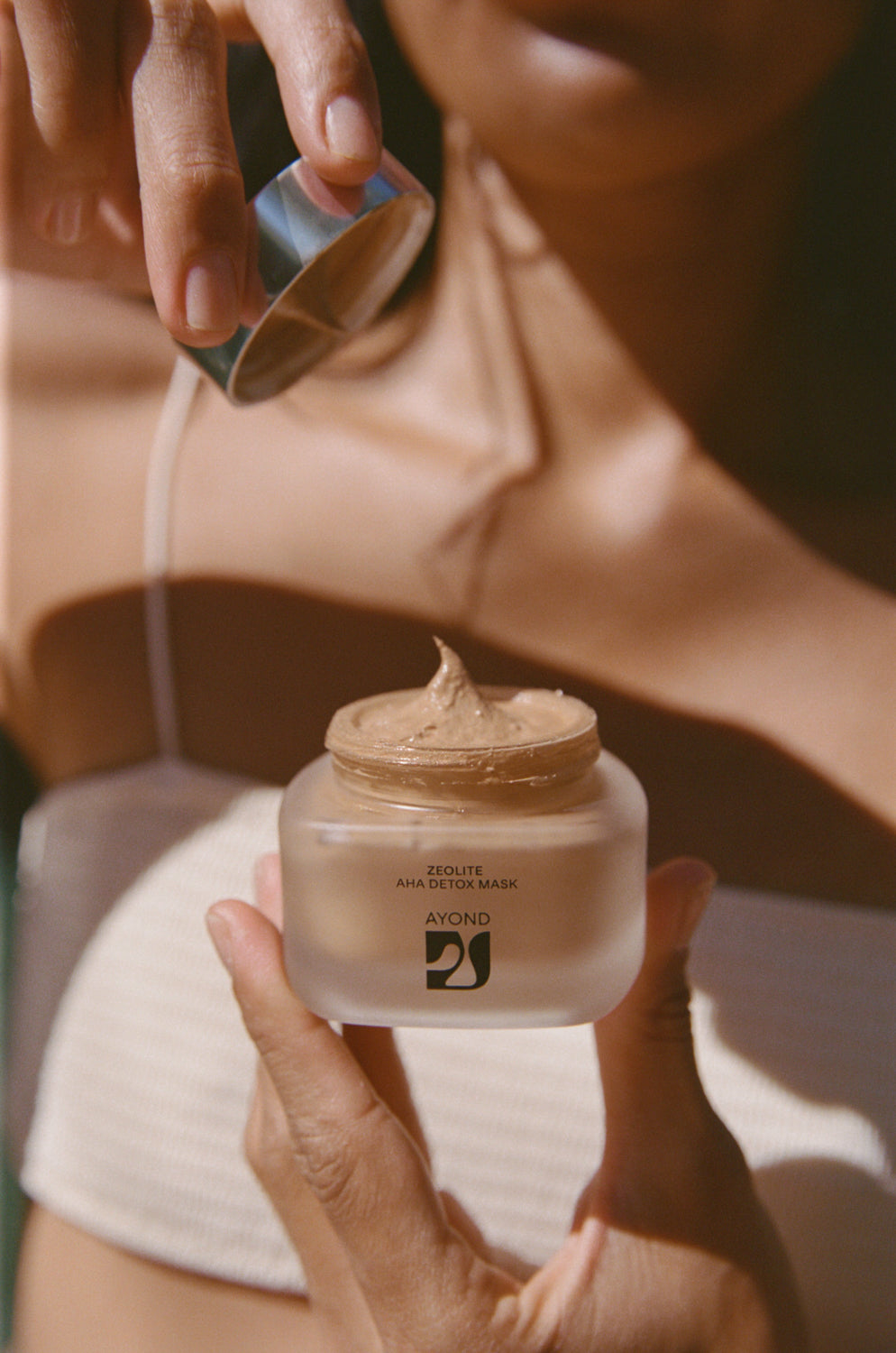 Hands scooping Zeolite AHA Detox Mask from the jar