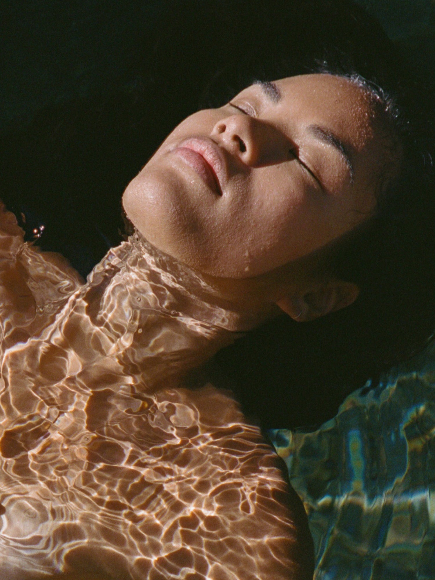 Person lying in water with sunlight filtering through, creating a serene atmosphere.